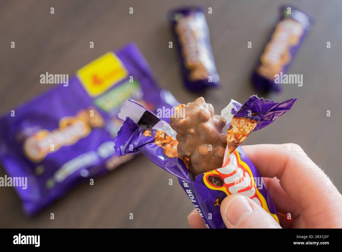 Una mano dell'uomo che tiene una barra di cioccolato del picnic di Cadbury unwrapped, circa mangiarla, Inghilterra. Concetto: Grasso e zucchero, snacking, cibo malsano Foto Stock