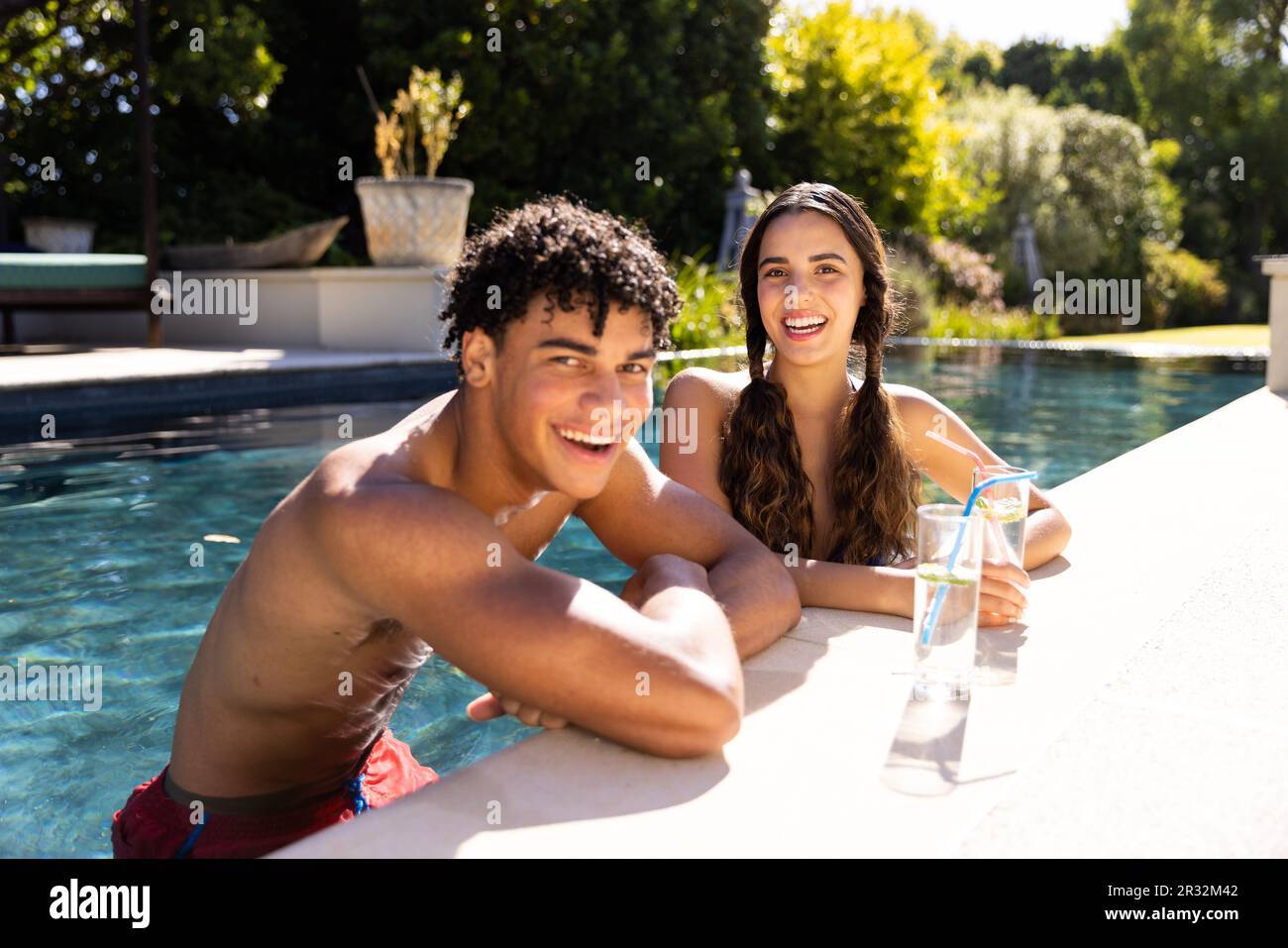 Ritratto di felice fit diverse coppie in piedi in piscina sorridendo al sole con cocktail Foto Stock