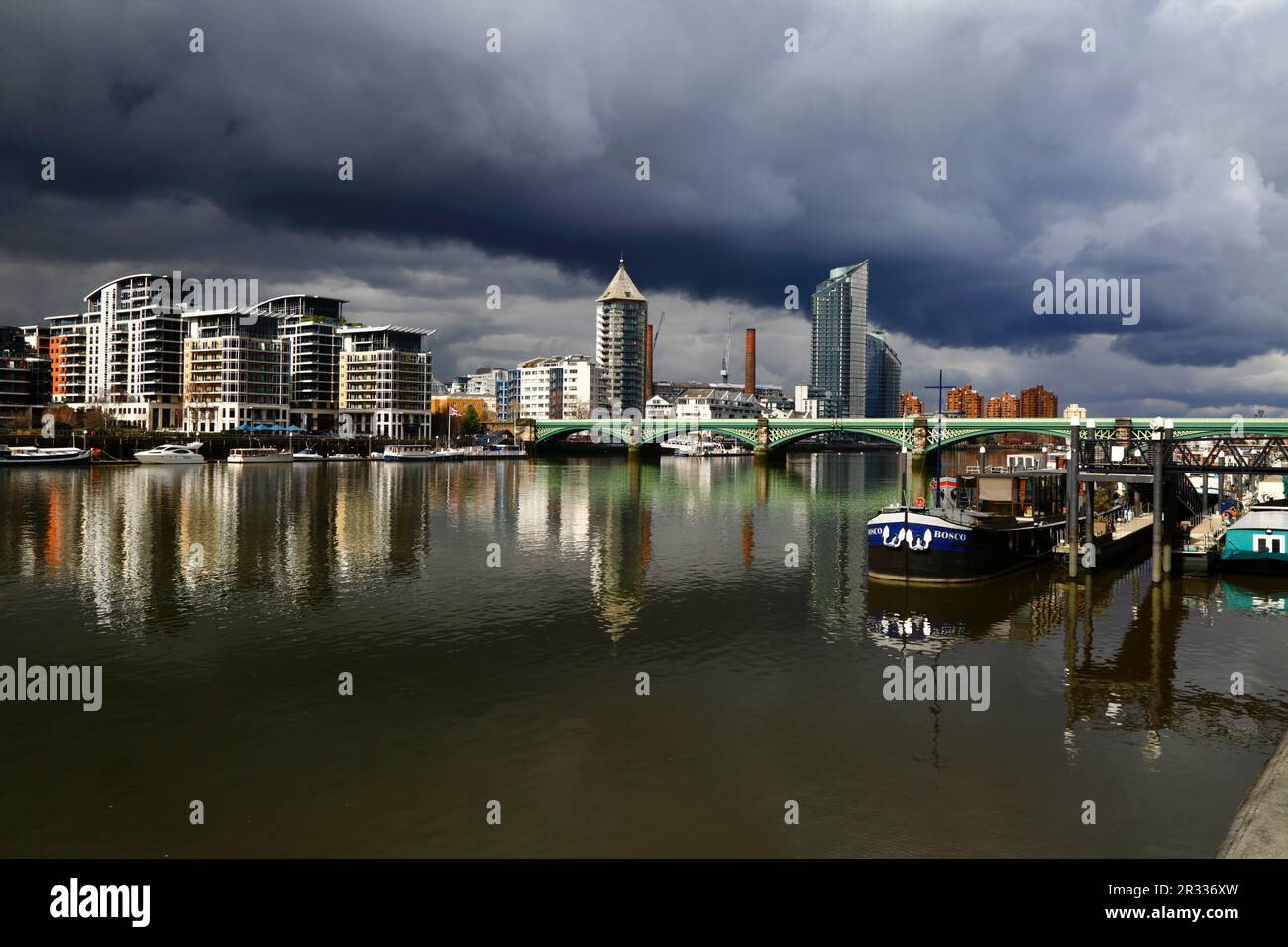 Battersea Railway Bridge / Chelsea River Bridge attraverso il Tamigi e la Torre Belvedere (Chelsea Harbour) sotto i cieli bui e tempestosi, Londra, Regno Unito Foto Stock