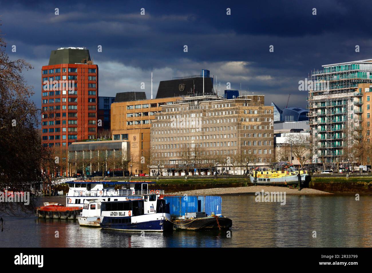 River Thames, Westminster Tower (L) e gli uffici dell'International Maritime Organization (al centro) sotto un cielo tempestoso, London Belle party boat in primo piano Foto Stock