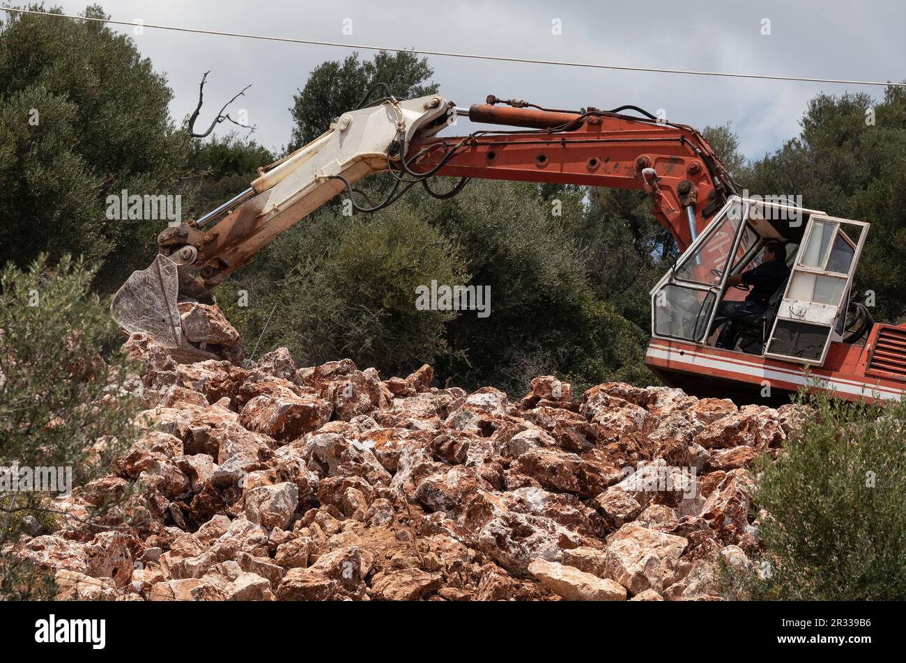 Creta, Grecia, Europa. 2023. Macchina escavatore che sposta rocce in una superficie piana per fondazioni di un edificio. Foto Stock