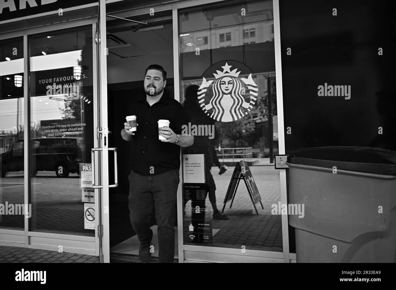Bianco e nero: Un uomo lascia la caffetteria Starbucks portando due tazze di caffè a Toronto, Canada Foto Stock