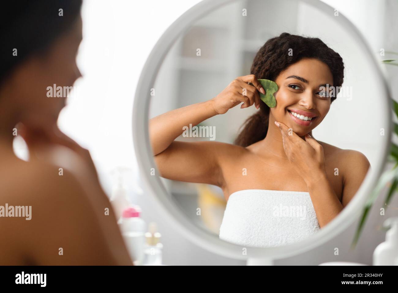 Bella giovane donna nera che fa il massaggio facciale con gua sha strumento Foto Stock