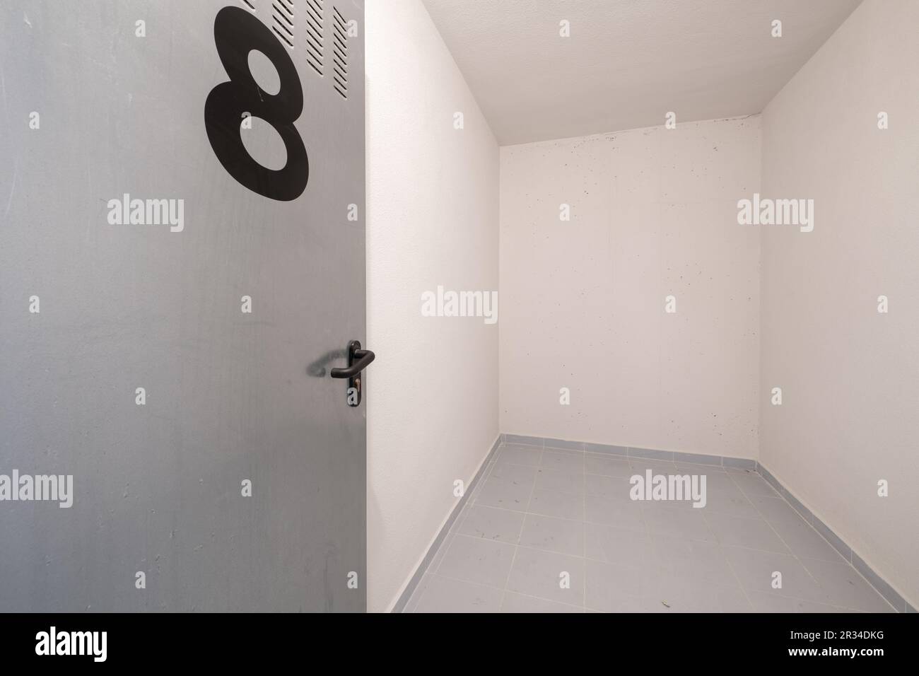 Un ripostiglio vuoto al piano terra di un edificio residenziale con pareti dipinte di bianco e pavimenti piastrellati grigi Foto Stock