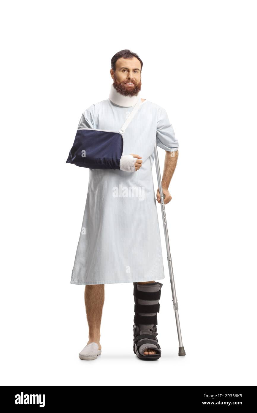 Uomo barbuto in un abito di ospedale con una gamba rotta, braccio e collo collare isolato su sfondo bianco Foto Stock