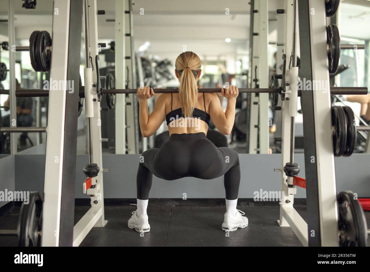 Immagine vista posteriore di una donna in forma che solleva una barra del peso in una palestra di fronte a uno specchio Foto Stock