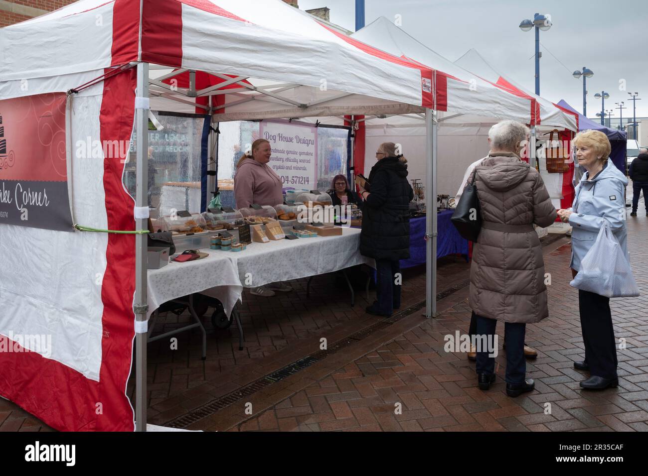 Casalinghe che chiacchierano sotto la pioggia di fronte alla stalla della torta del Nicolò nel mercato settimanale di Redcar Foto Stock