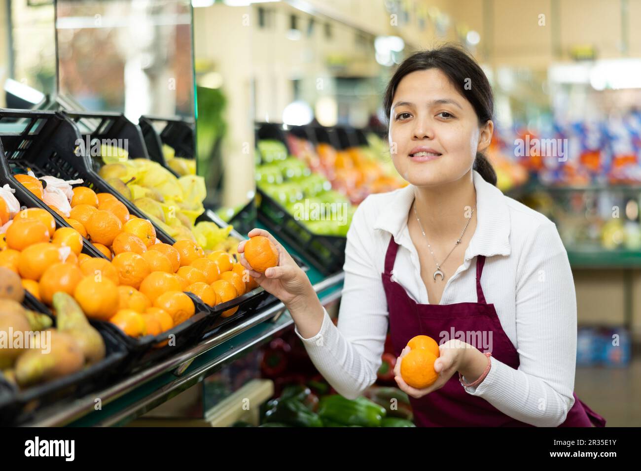Asiatico donna venditore in grembiule sceglie mandarino maturo Foto Stock