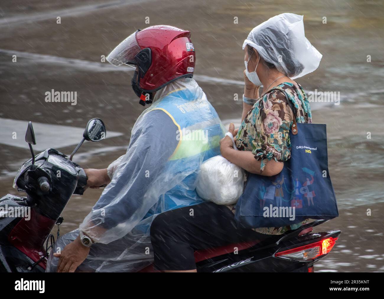 SAMUT PRAKAN, THAILANDIA, 10 2023 MAGGIO, Un moto-taxi guida con un passeggero sotto la pioggia Foto Stock