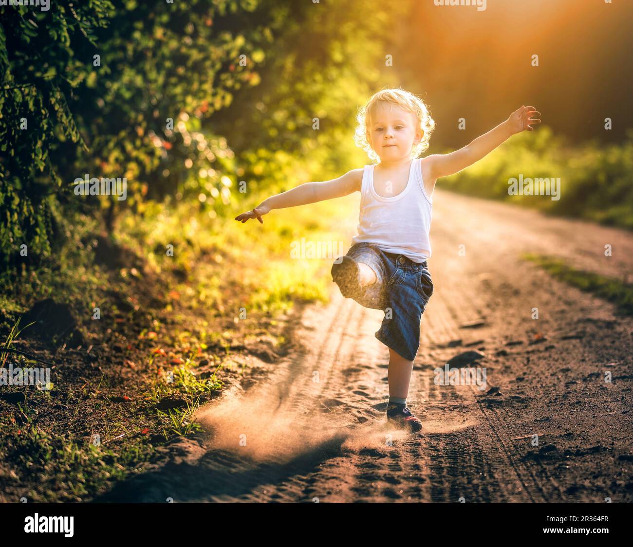 Ragazzo che gioca sulla strada rurale di campagna. Ragazzo blonde che gioca con la sabbia. Foto Stock