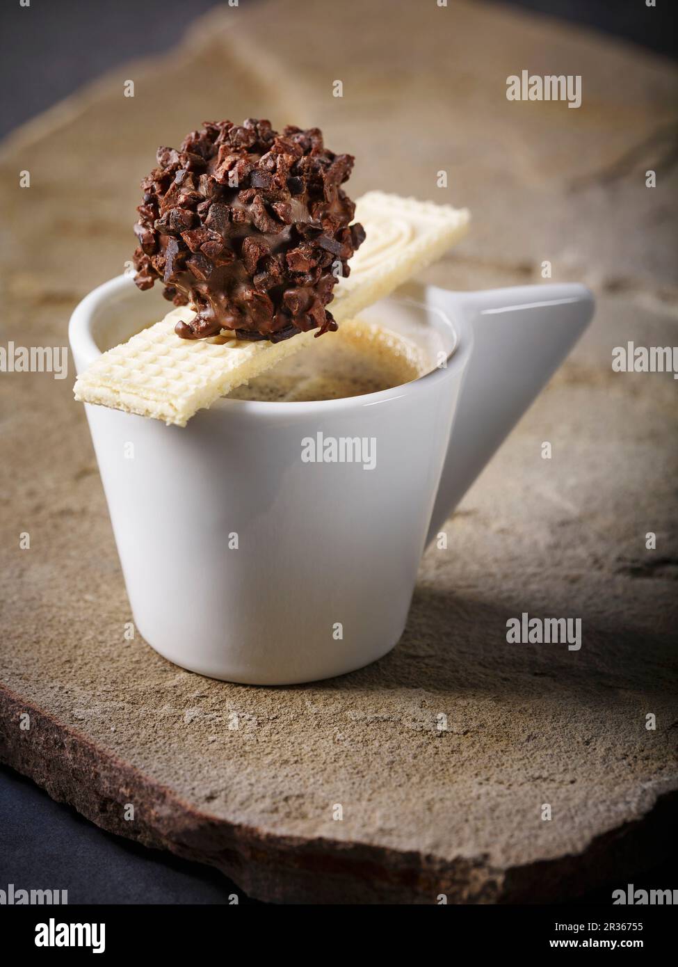 Un tartufo di torrone fatto in casa in cioccolato fondente con schegge di cacao su una tazza di espresso con un wafer Foto Stock