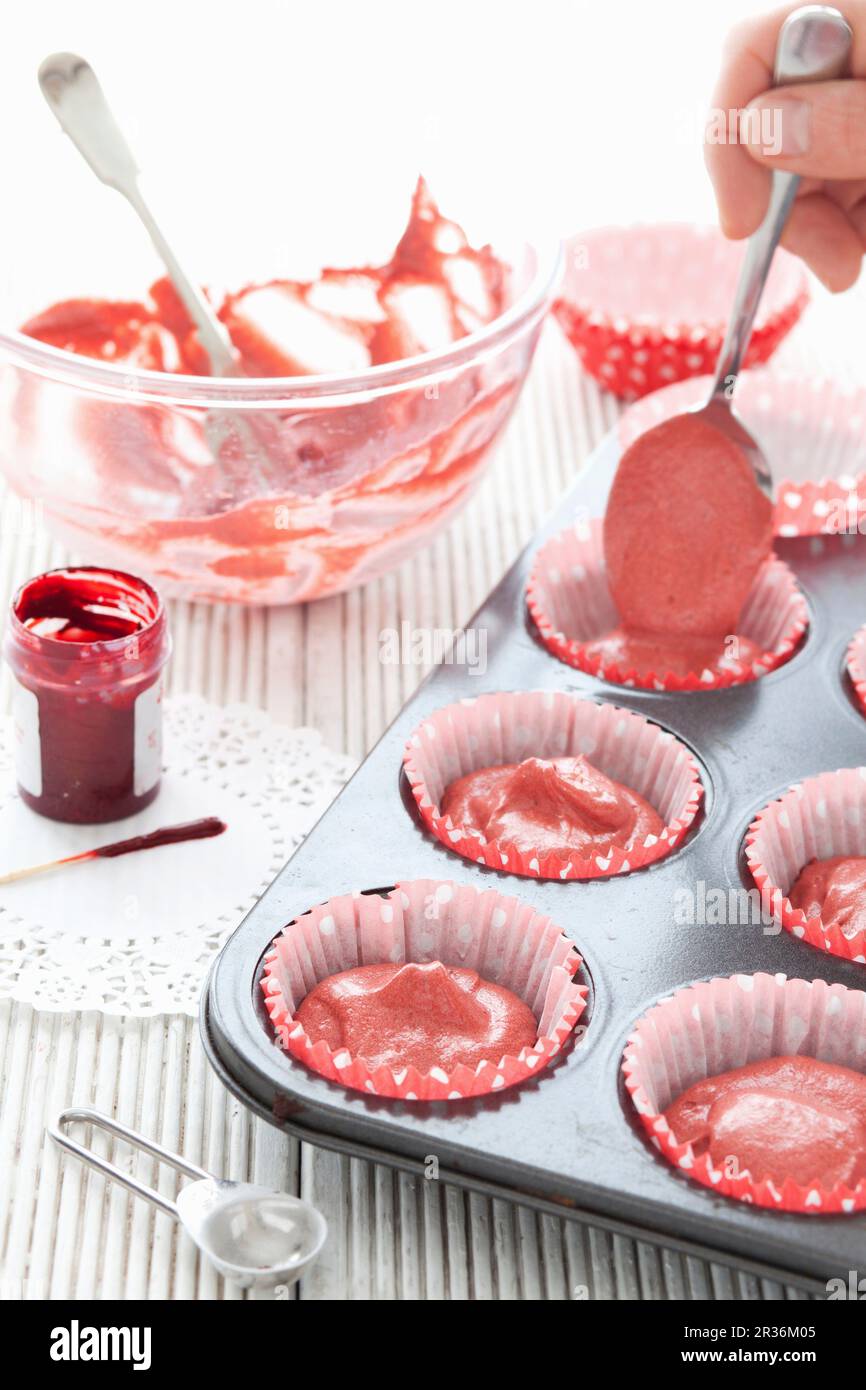 Pastella di torta di velluto rosso che è riempita in casse di cupcake di carta Foto Stock