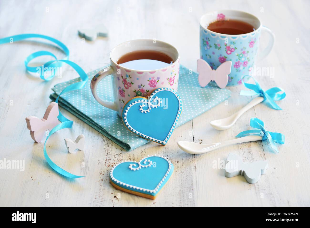 A forma di cuore biscotti decorate con blu e bianco ghiaccio e servito con due tazze di tè Foto Stock