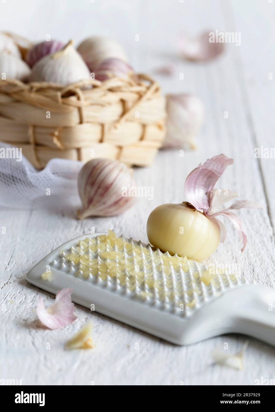 Sbucciate singolo spicchio d aglio grattugiato su un bianco di ceramica grattugia con un cesto di paglia pieno di non pelati singolo spicchio garlics Foto Stock