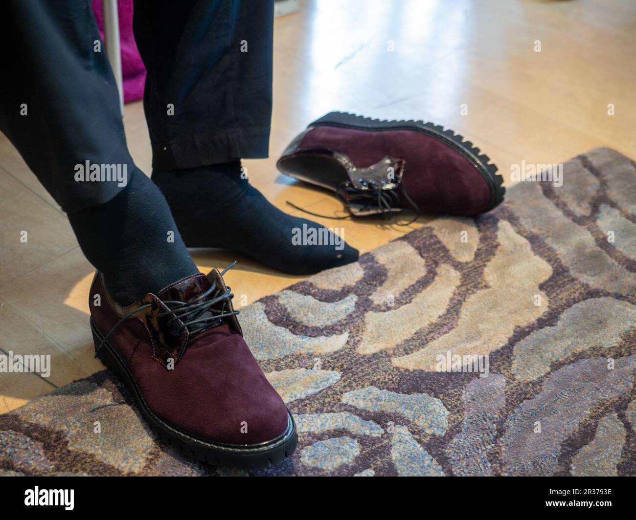 donna irriconoscibile nel negozio cercando nuove scarpe. Donna caucasica seduta in un negozio di scarpe mentre sceglie nuovo paio di sneakers italiani. Foto Stock