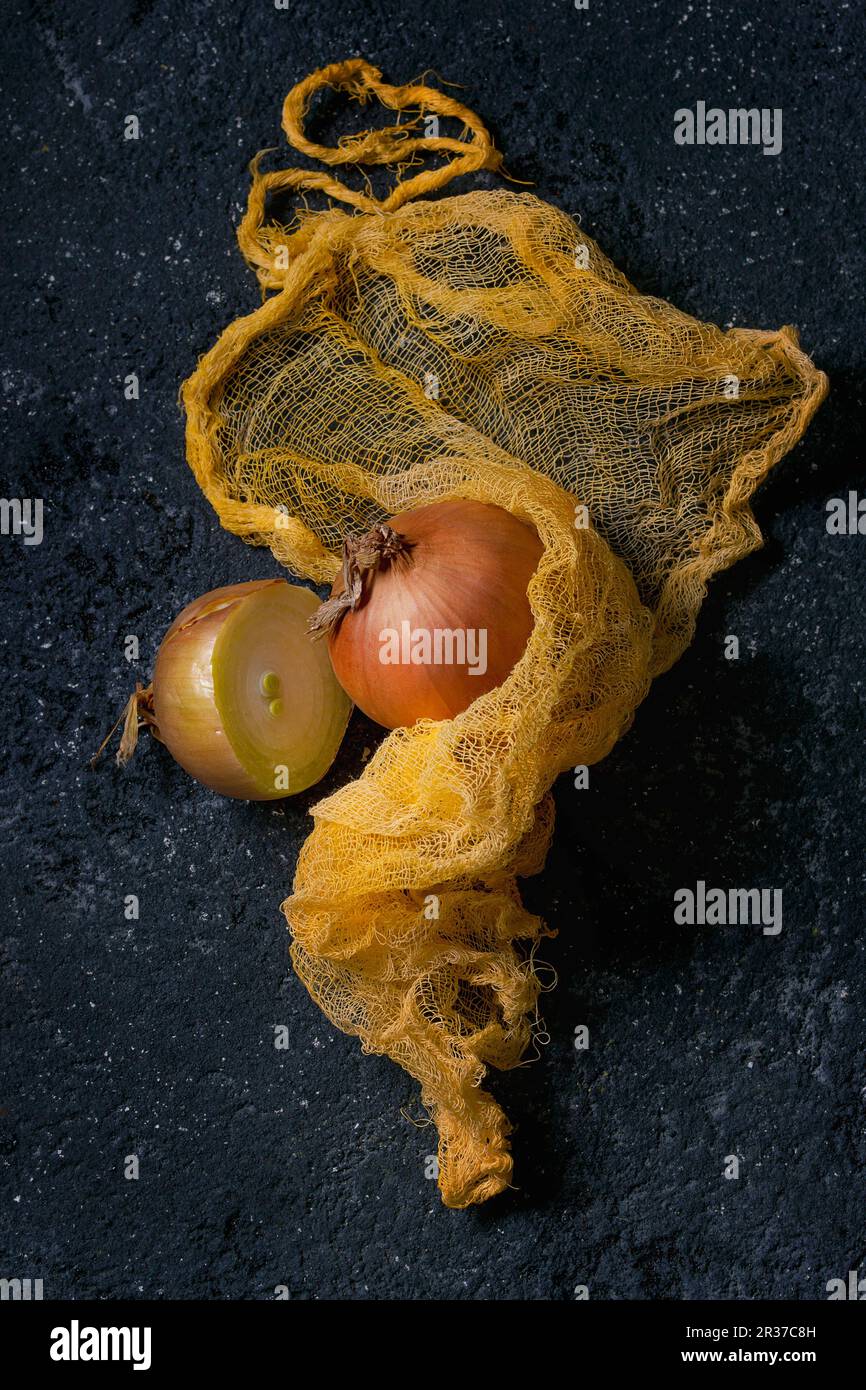 Cipolle intere e metà gialle in straccio giallo su fondo di pietra nera Foto Stock