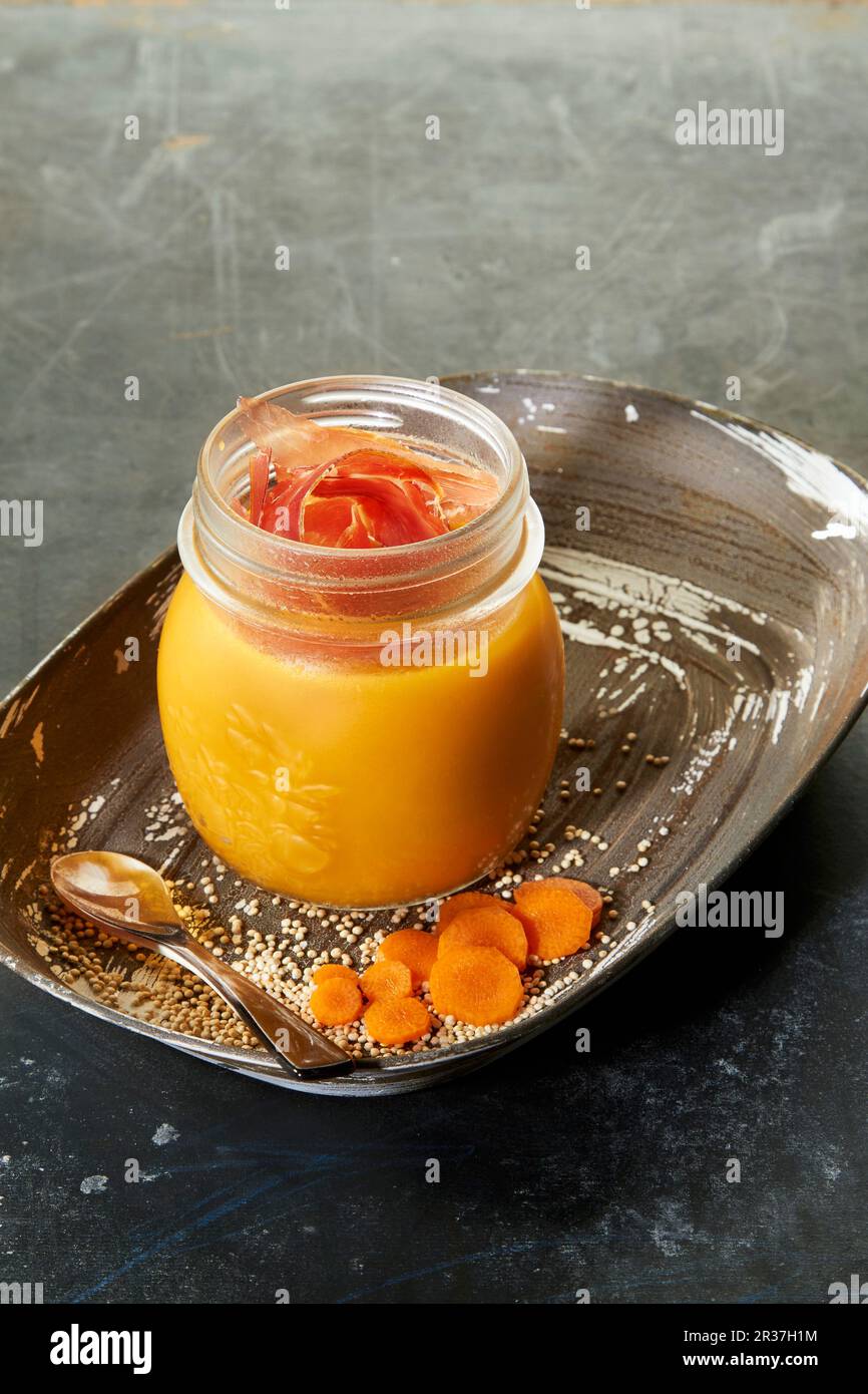 Cremosa di carota e la quinoa minestra con prosciutto crudo in un vasetto di vetro Foto Stock