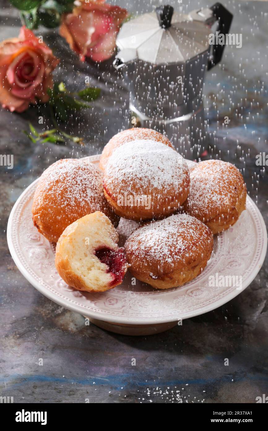 Lo zucchero a velo viene setacciato su un piatto di ciambelle di marmellata Foto Stock