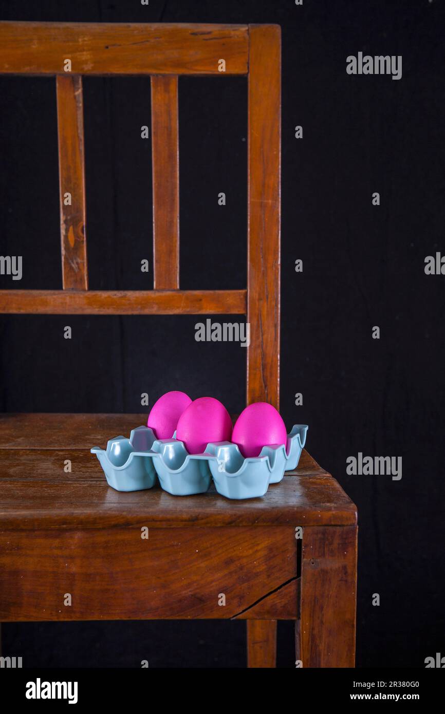 Uova rosa di Pasqua in un cartone di uova su una sedia di legno Foto Stock