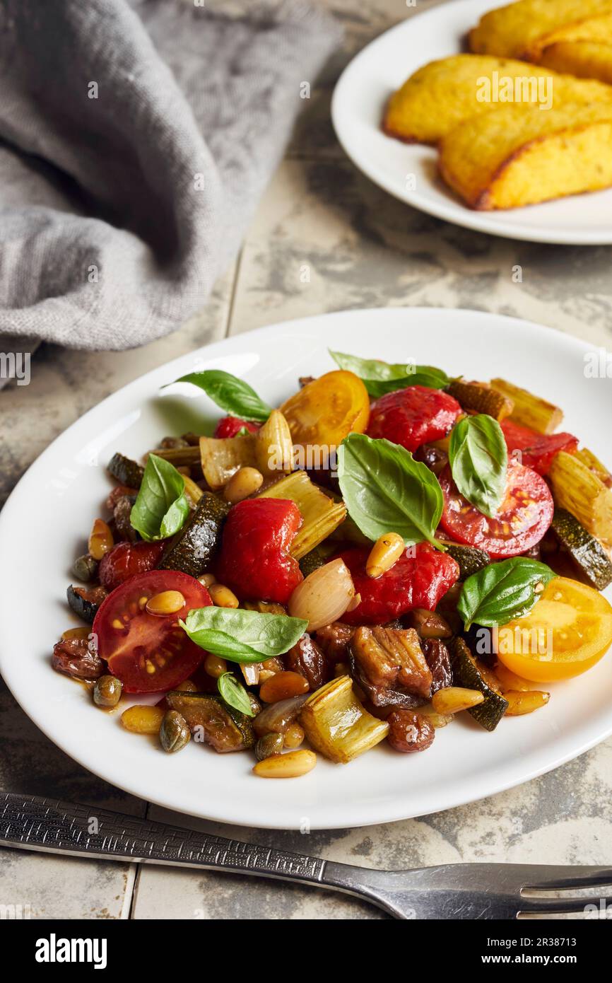 Caponata con peperoni e pomodori ciliegini serviti con fette di polenta Foto Stock