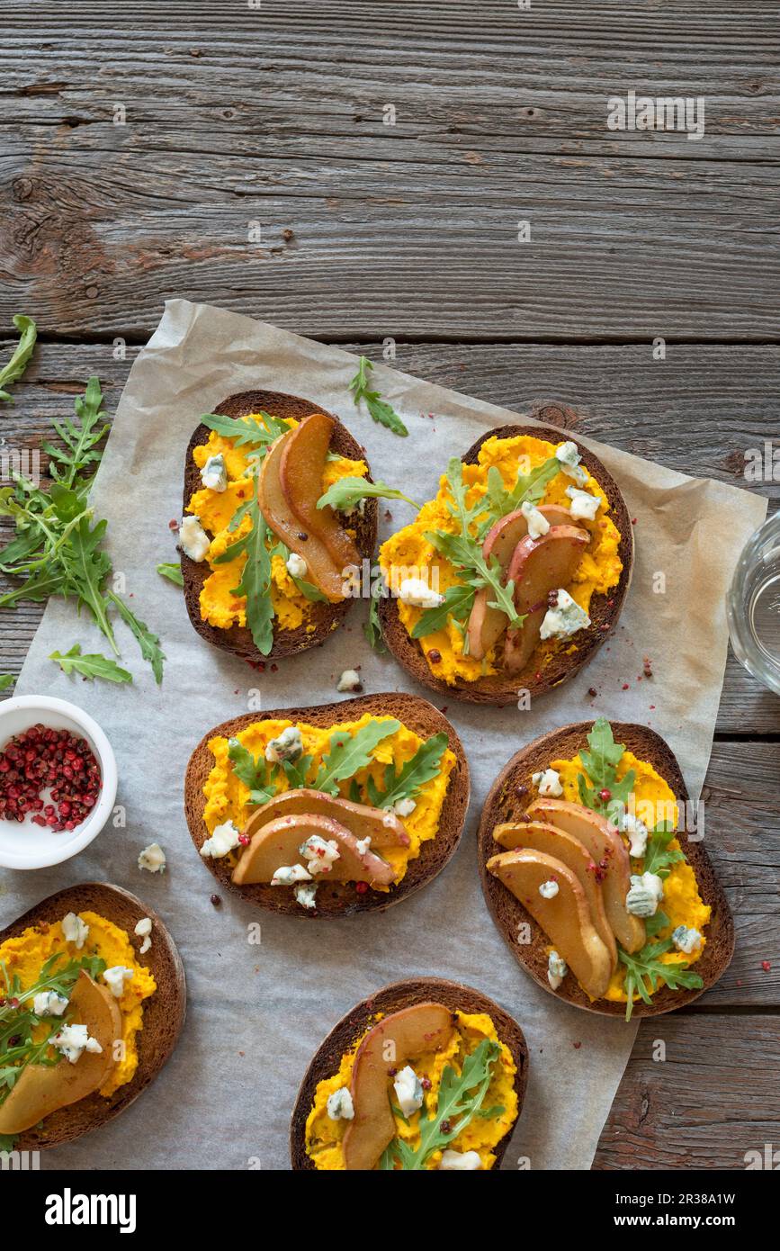 Crostini con ricotta di zucca, pere arrosto, formaggio azzurro e rucola Foto Stock