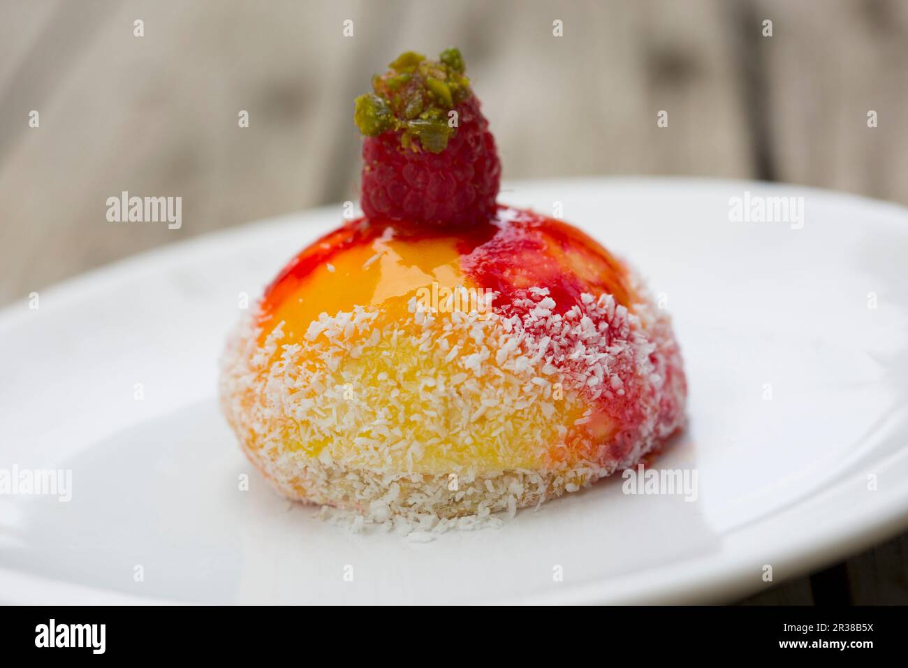 Un mango e mousse al frutto della passione su una sfoglia di pasta con cocco grattugiato condito con un lampone e un trito di pistacchi di Bronte su una piastra bianca Foto Stock