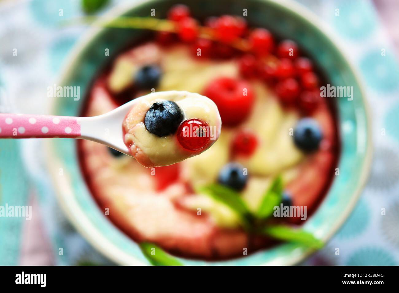 Crema con frutta fresca e sciroppo di frutta su un cucchiaio sopra una ciotola Foto Stock