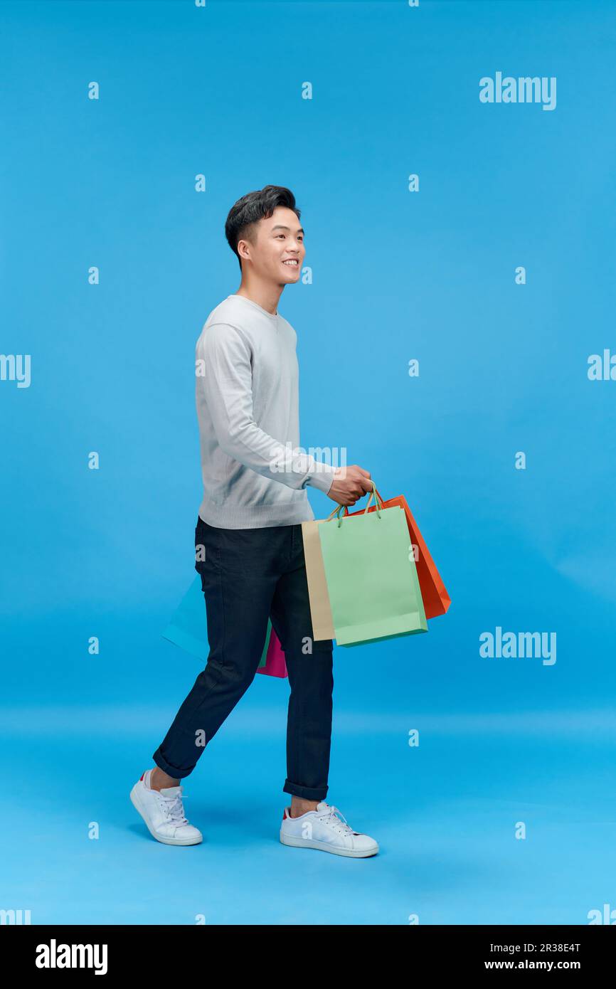 uomo felice sorriso positivo andare a piedi passo shopping borse isolato su sfondo blu Foto Stock