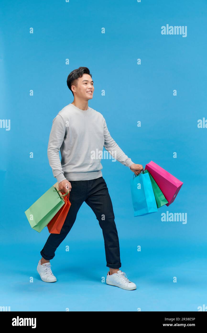 uomo felice sorriso positivo andare a piedi passo shopping borse isolato su sfondo blu Foto Stock