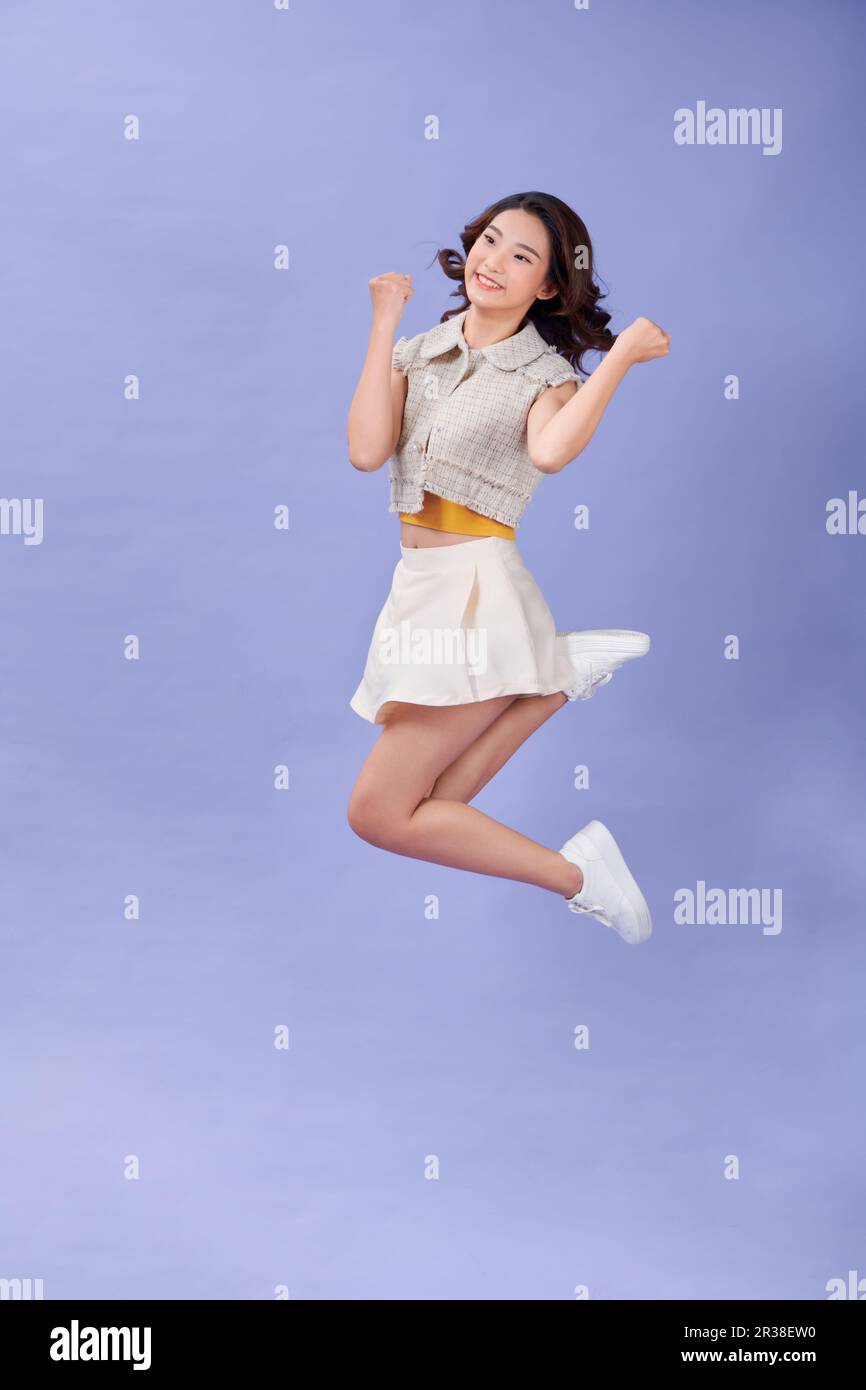 Lunghezza intera di giovane donna allegra che salta alto sorridente mostrando i muscoli di alimentazione isolati su sfondo viola Foto Stock