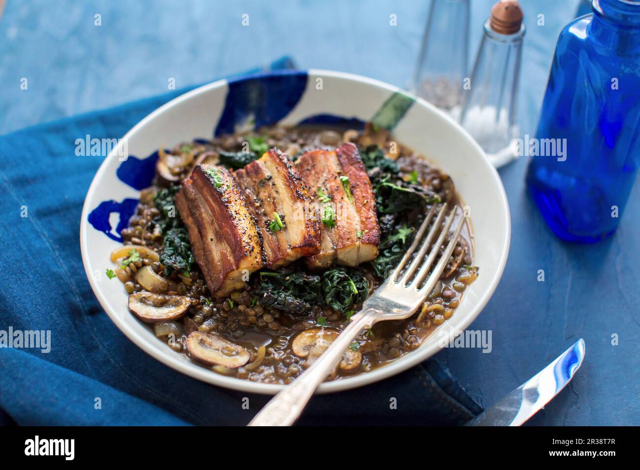 Pancia di maiale su lenticchie con funghi e cavolo Foto Stock