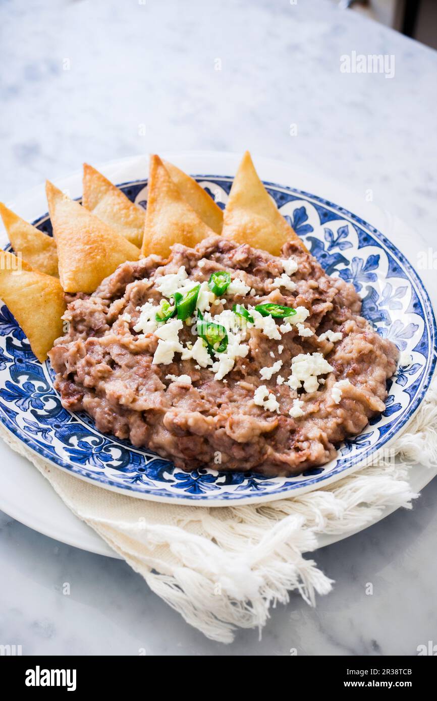 Un piatto con fagioli di pinto fritti guarniti con formaggio fresco, peperoncino verde e tortilla fritta di mais (totopos) Foto Stock