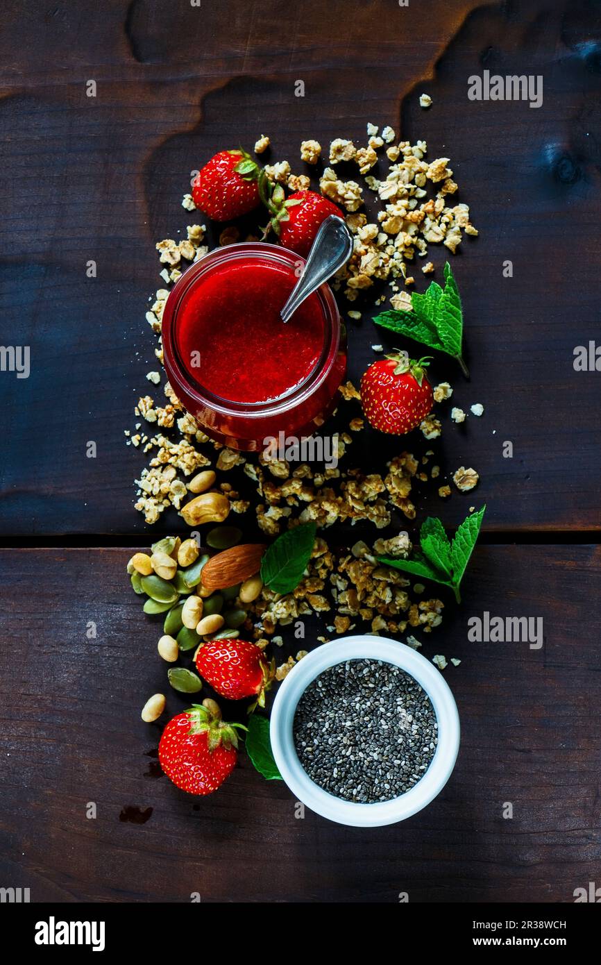 Purea di fragole appena sfornata, semi di chia, muesli, frutti di bosco freschi e menta per colazione o frullato. Ingredienti sani su sfondo di legno scuro Foto Stock