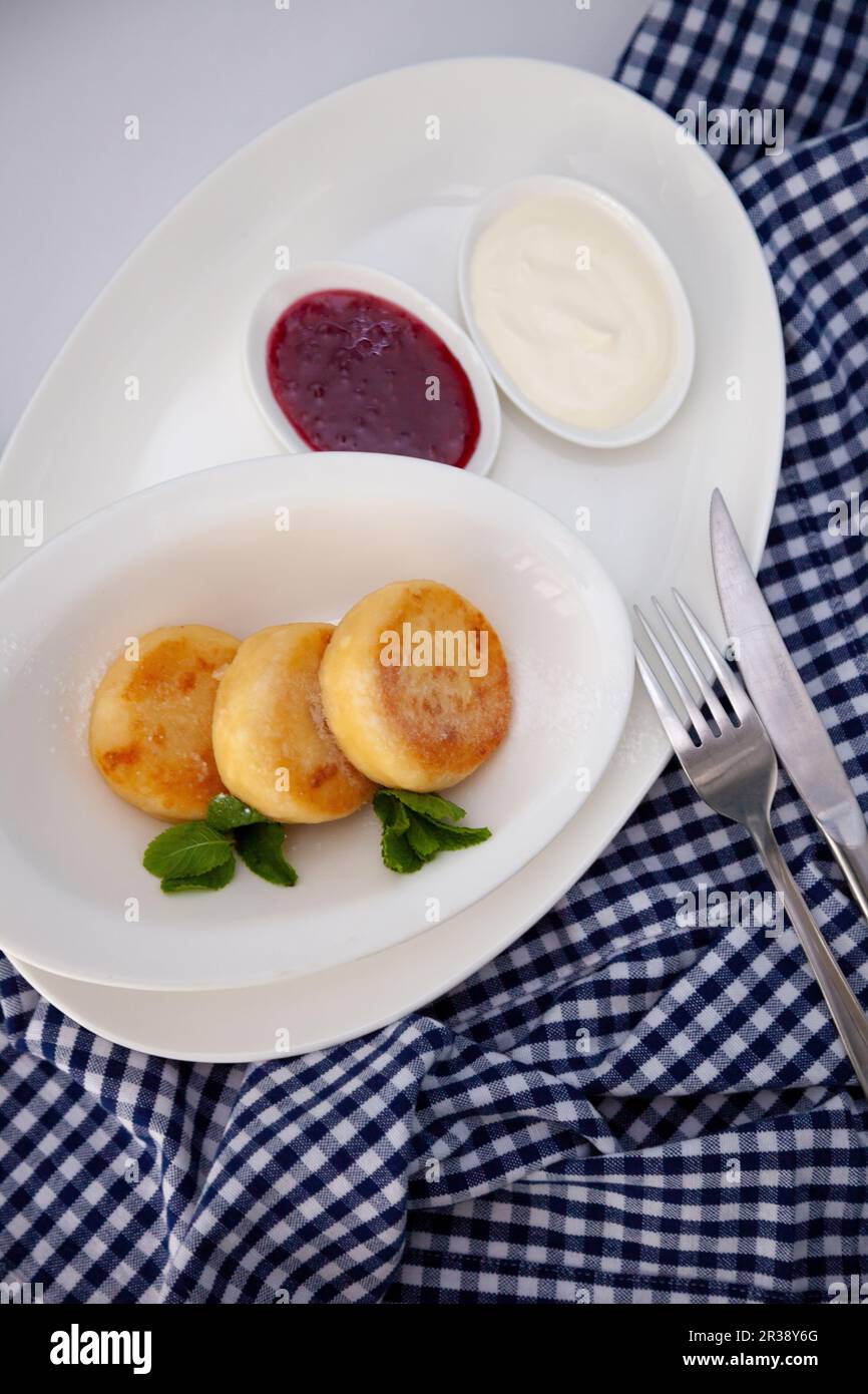 Frittelle di formaggio ricotta rotonda in un piatto bianco su sfondo blu. Cibo prima colazione. Cibo sano. Salsa di panna acida e menta. Primo piano vista dall'alto. Pasto dessert. Frittelle di ricotta al formaggio ricotta. Foto Stock