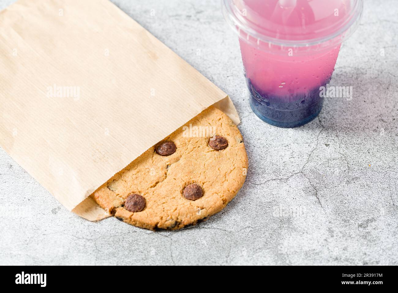 Biscotto con scaglie di cioccolato avvolto in sacchetto di carta con bevanda accanto su un tavolo di pietra Foto Stock