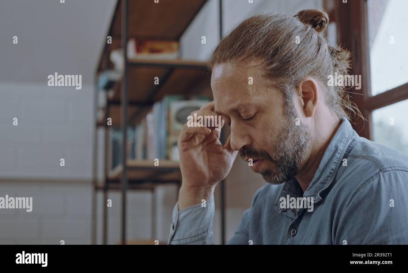 Un giovane uomo preoccupato che usava un computer portatile seduto sul letto in camera da letto. Foto Stock