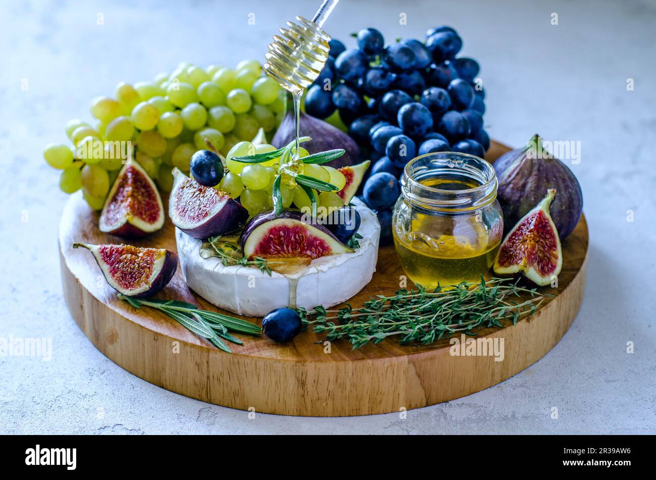 Formaggio Camembert con fichi, miele, uva ed erbe aromatiche su un tagliere Foto Stock