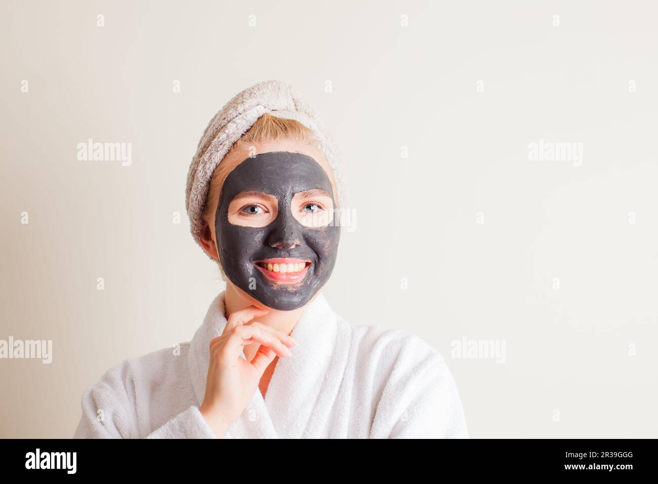 Ridendo la ragazza giovane con un asciugamano sulla sua testa usando una maschera nera sul suo viso Foto Stock