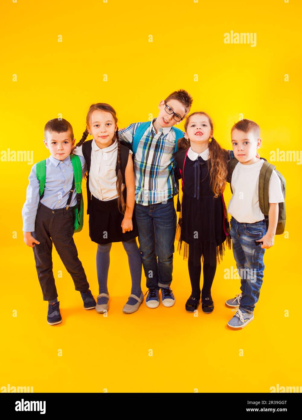 Gruppo di bambini felici della scuola che abbracciano e stanno insieme in tutta la lunghezza sullo sfondo giallo Foto Stock