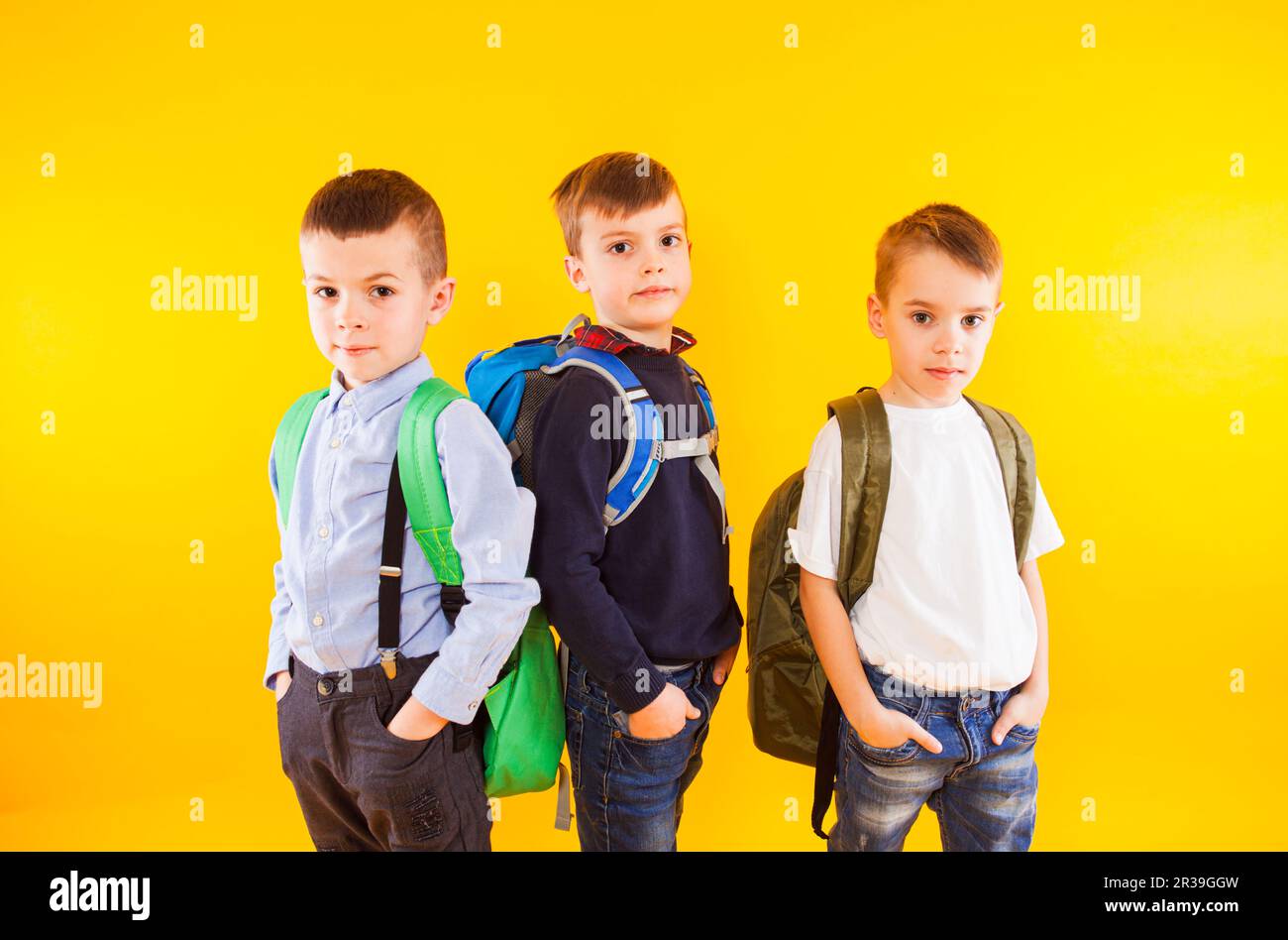 Graziosi scolari in uniforme con zaini su sfondo giallo Foto Stock
