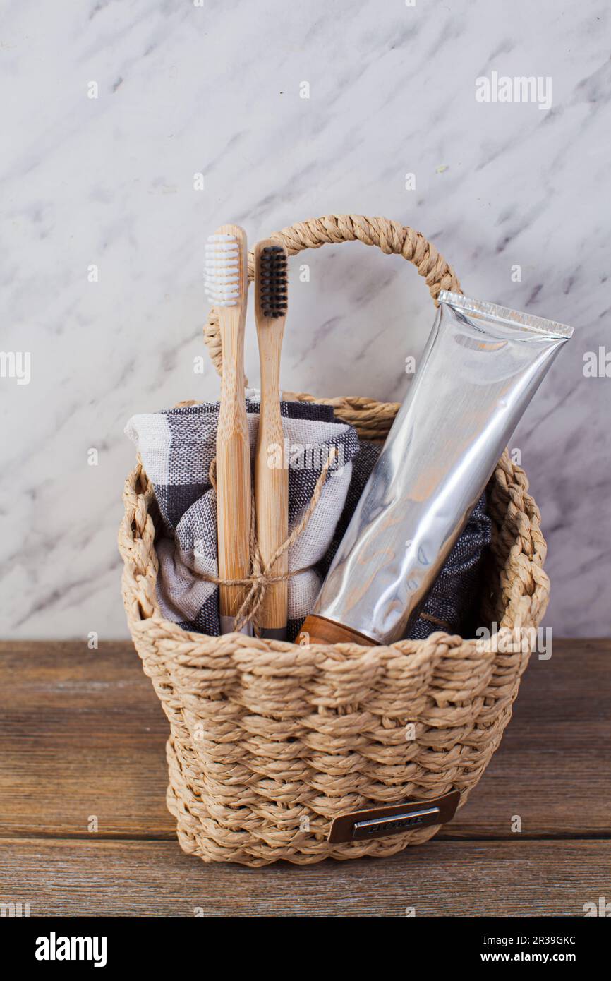 Spazzolini da denti in bambù naturale eco e dentifricio organico in un cesto in bagno. Foto Stock