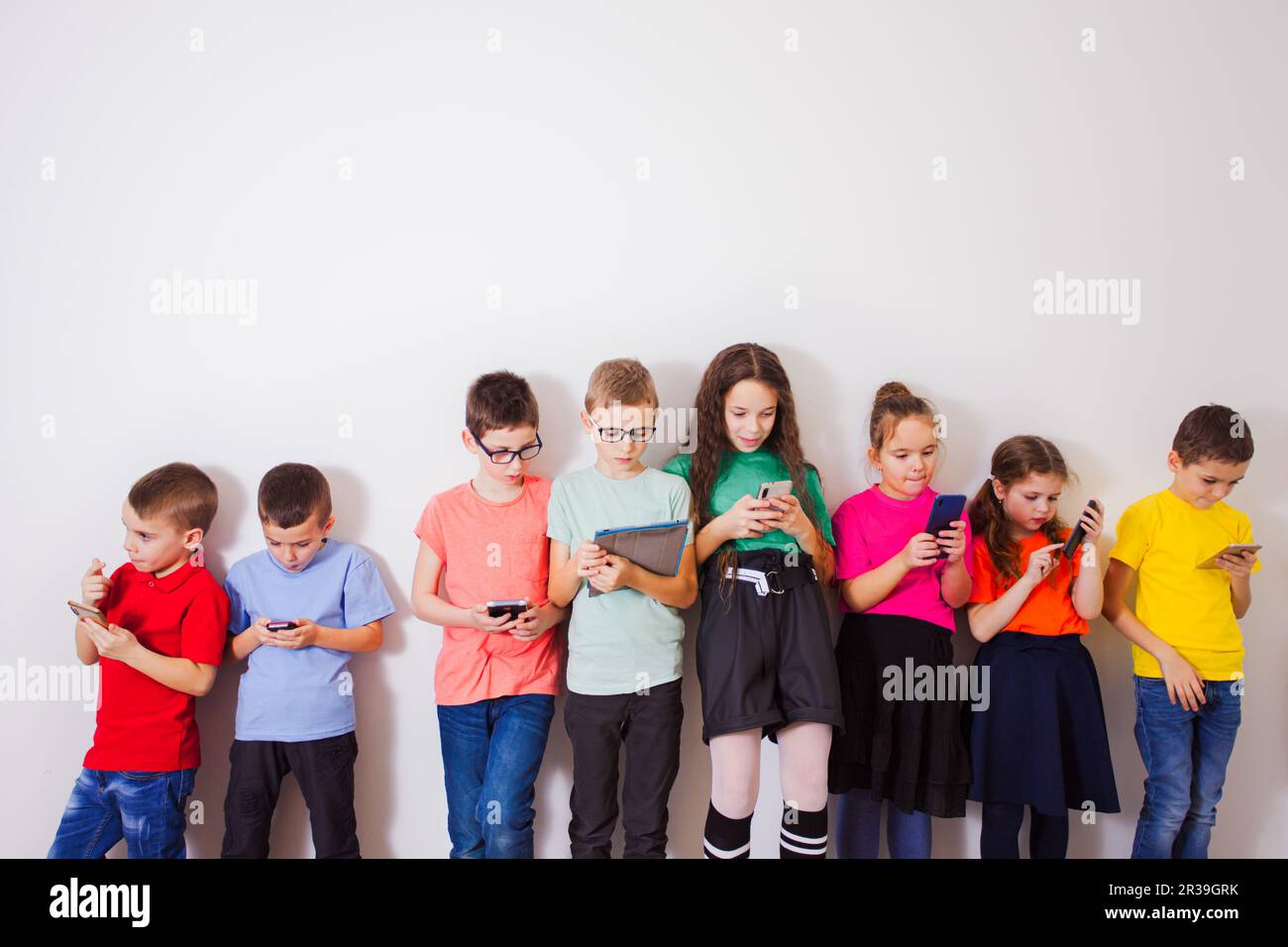 Gruppo di studenti di scuole elementari felici con smartphone su muro bianco Foto Stock