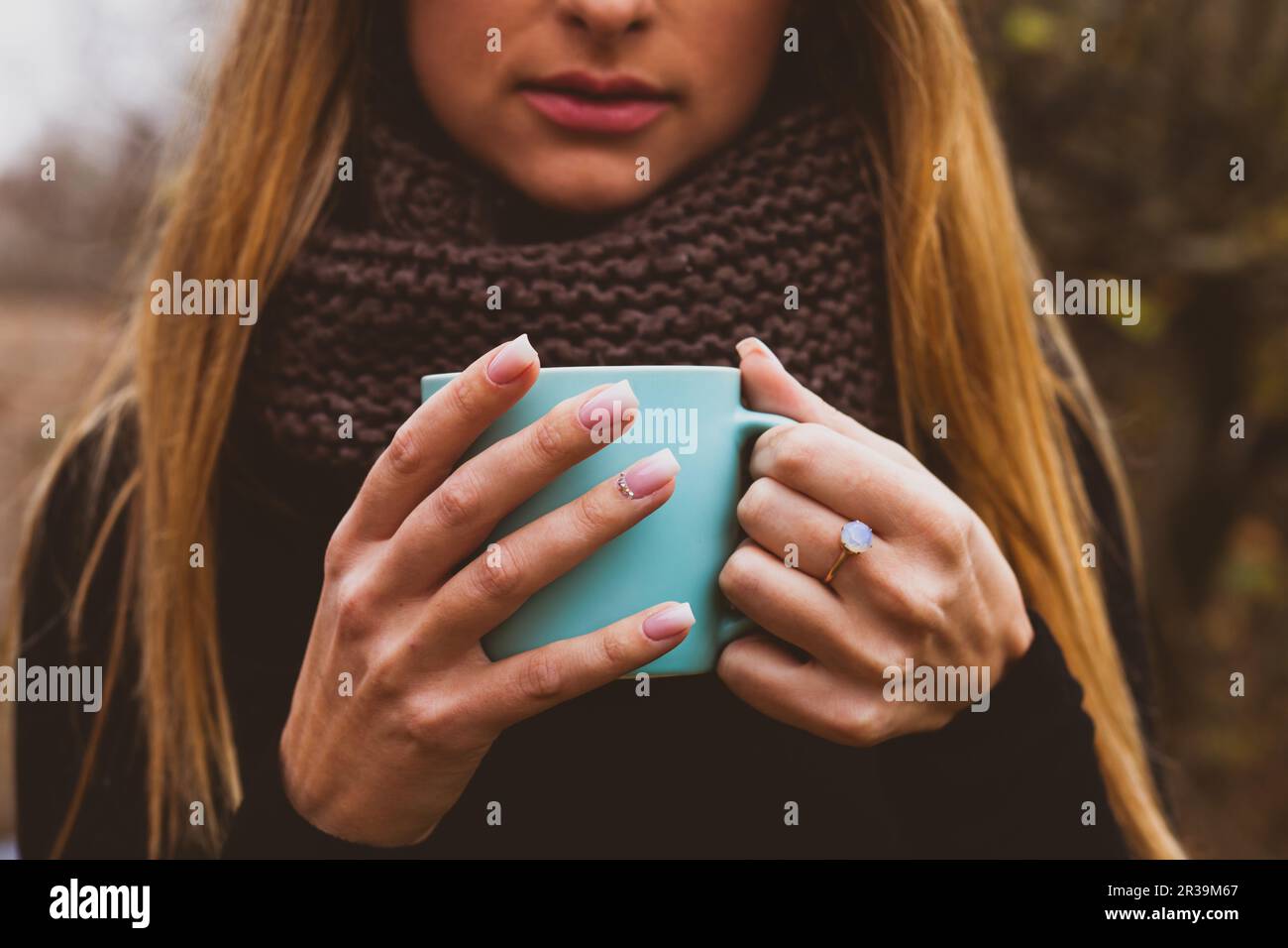 Le mani femminili con il disegno tenero del chiodo rosa che tiene la tazza blu all'aperto. Donna bellezza e benessere. Foto Stock