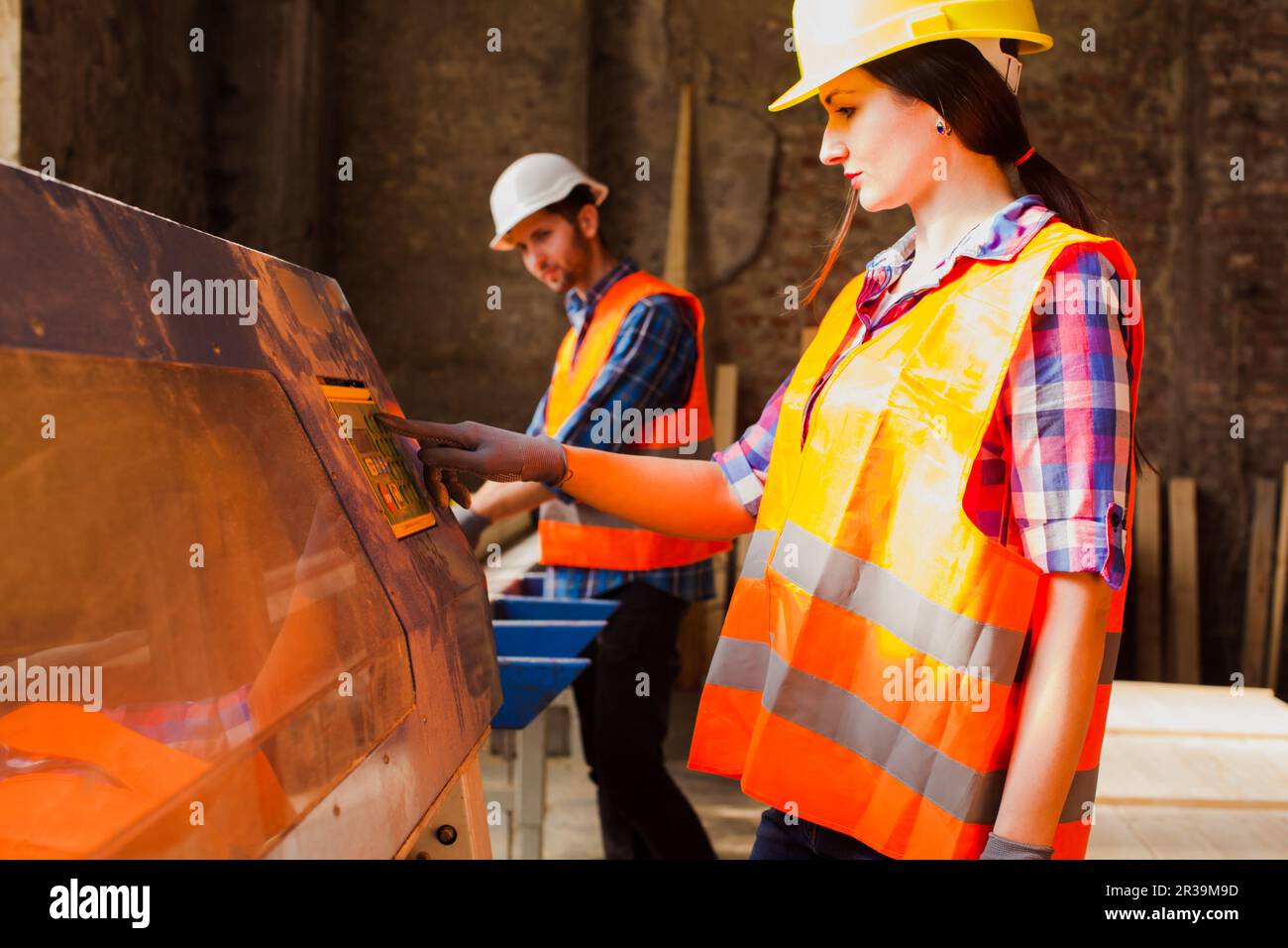 Donna di lavoro in casco protetto e vestiti premendo il pulsante sulla macchina per la lavorazione del legno. Foto Stock