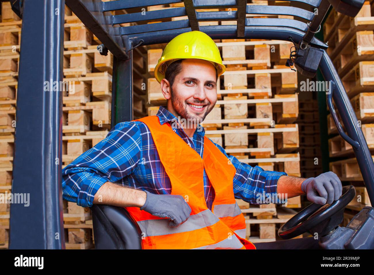 Bel lavoratore sorridente che guida carrello elevatore in magazzino. Concetto di industria della lavorazione del legno. Foto Stock