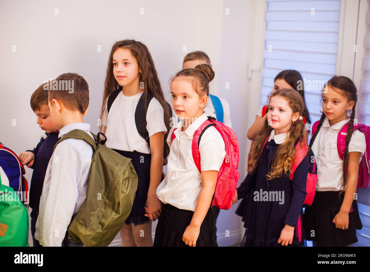 Bambini in uniforme con zaini che vanno in classe Foto Stock
