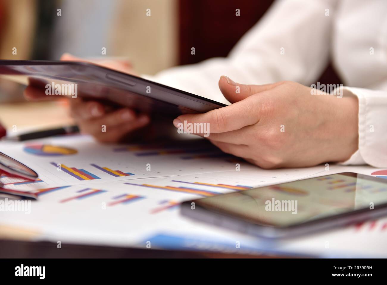 Donna d'affari seduta in ufficio con un tablet. Grafici di reddito e grafici a tabella. Foto Stock