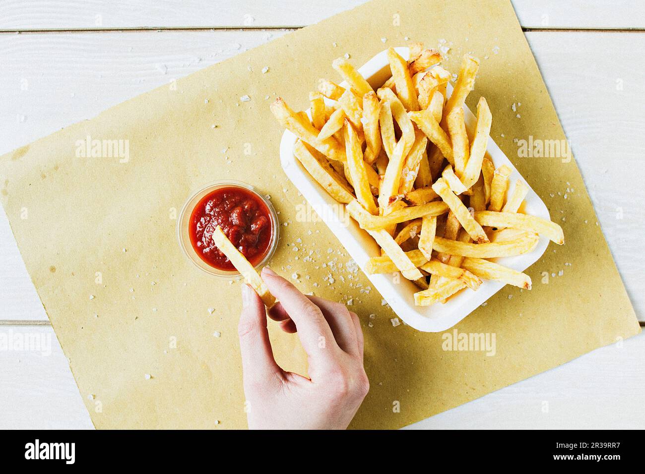 Una porzione di patatine fritte con sale marino, con una mano immersione in ketchup Foto Stock