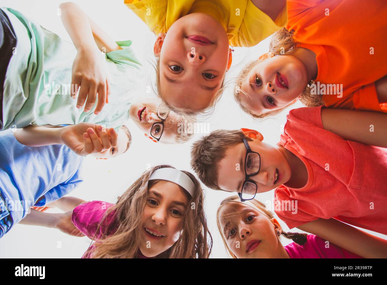 Squadra di bambini sorridenti che si abbracciano insieme in un cerchio, vista dal basso. Foto Stock
