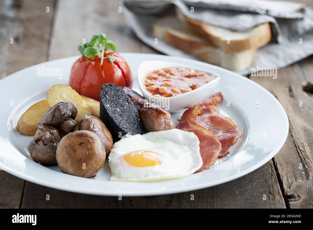 Colazione all'inglese servita su un piatto bianco con pane bianco affettato sullo sfondo Foto Stock